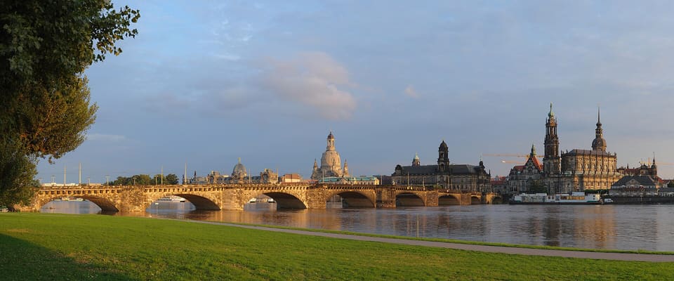 Pískovcový most Augustusbrücke o mnoha obloucích přes Labe ve večerním světle, za ním panorama starého města s kupolí Frauenkirche a věží Hofkirche, při pohledu z louky na břehu Neustadt.