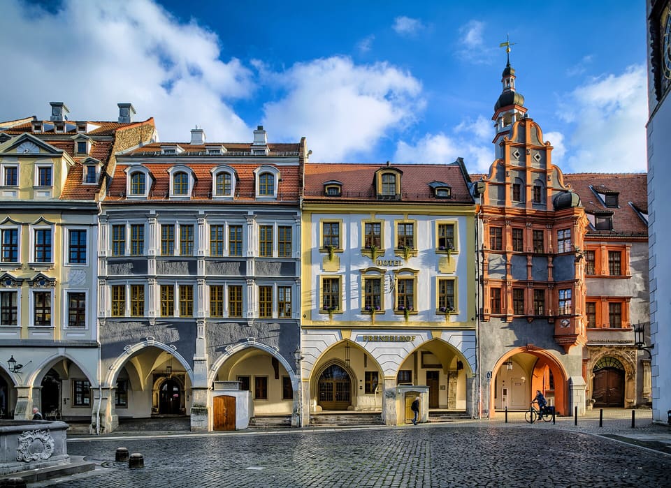 Řada barevných štítových domů s podloubím podél západní strany Untermarktu, dlážděného náměstí, pod modrou oblohou s bílými mraky.