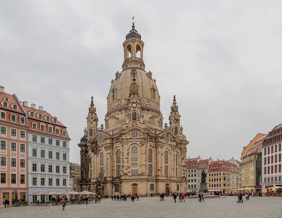 The Frauenkirche's sandstone dome and two stair towers rising above the cobbled Neumarkt, with colourful townhouses on either side under an overcast sky.