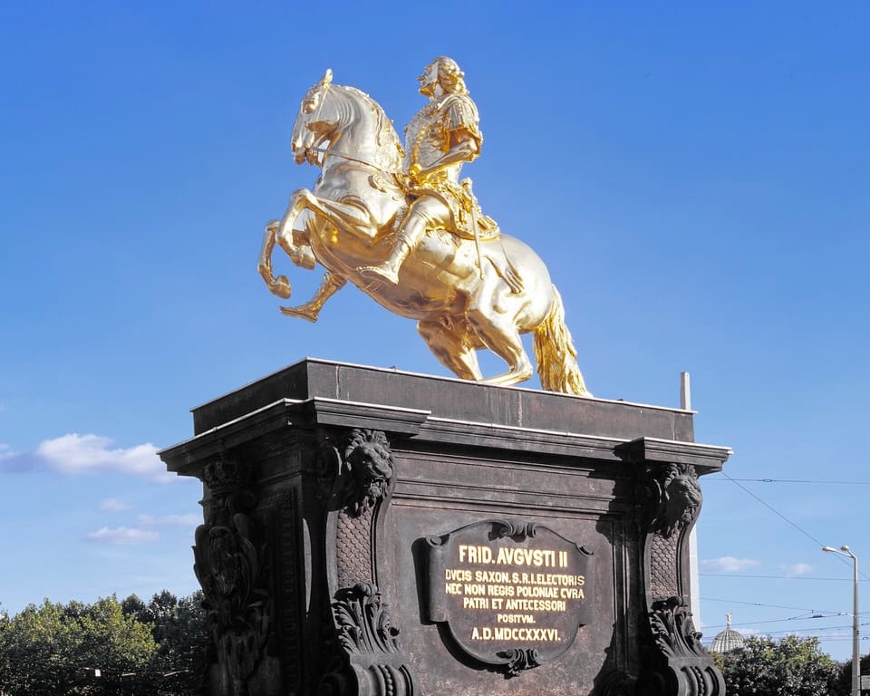 The gilded equestrian statue of Augustus the Strong on its dark stone plinth, with a gold Latin inscription on the front, against a blue sky.