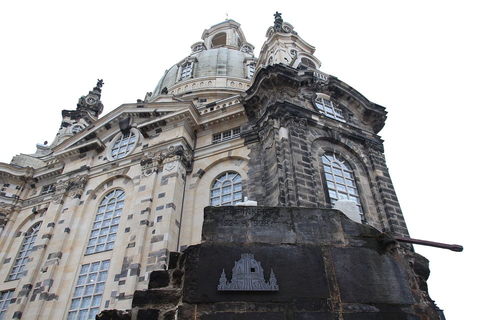 Looking up at the Frauenkirche's dome and walls, pale new sandstone patched with darker old stones, above a weathered block of dark masonry in the foreground.