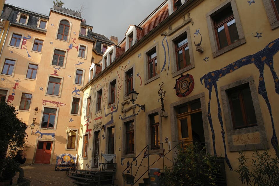 Dziedziniec Kunsthofpassage ze ścianami domów pokrytymi malowanymi postaciami, dużym niebieskim zwierzęciem na fasadzie po prawej, gwiazdami i ozdobionymi oknami.