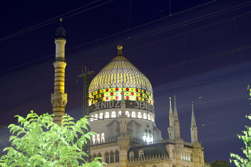 The Yenidze's glass dome glowing in yellow and blue with red rosettes, the striped minaret chimney at the left, against a dark blue night sky.