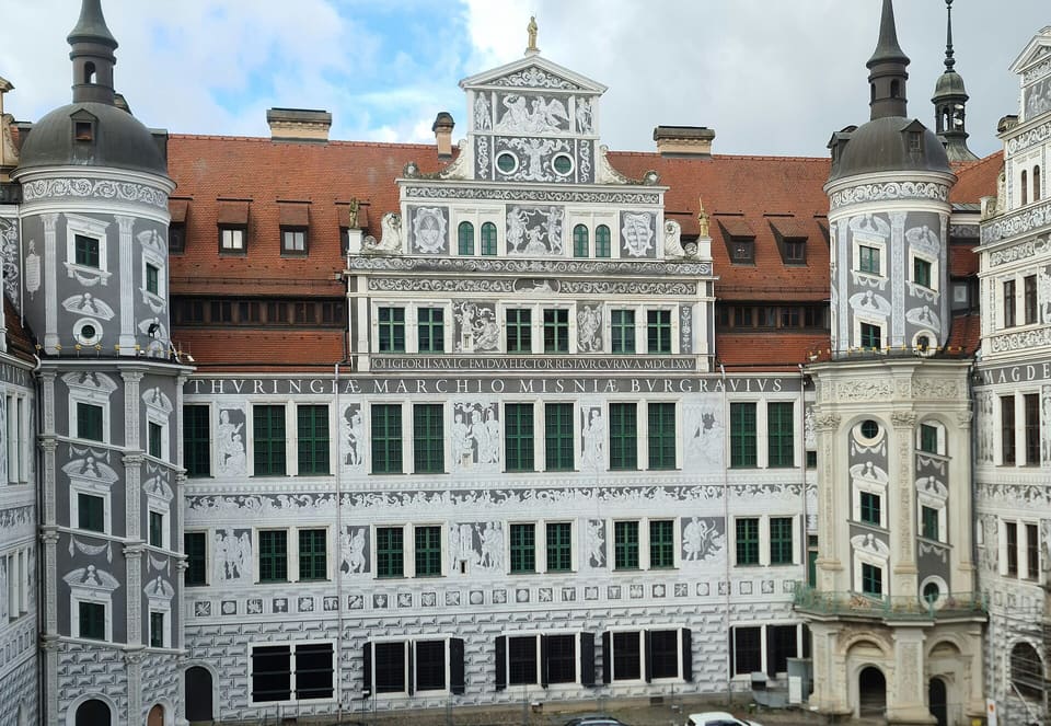 The grey and white sgraffito-patterned facade of the Residenzschloss's Great Courtyard, with its red roof, a gabled centre and two round corner turrets.