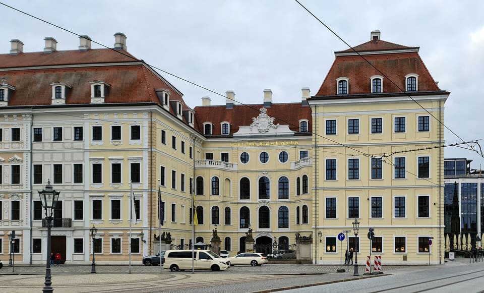 Světle žluté a bílé barokní průčelí Taschenbergpalais s červenou mansardovou střechou, zakřiveným středním křídlem a řadami vikýřů, při pohledu přes ulici s lampami a auty vpředu.
